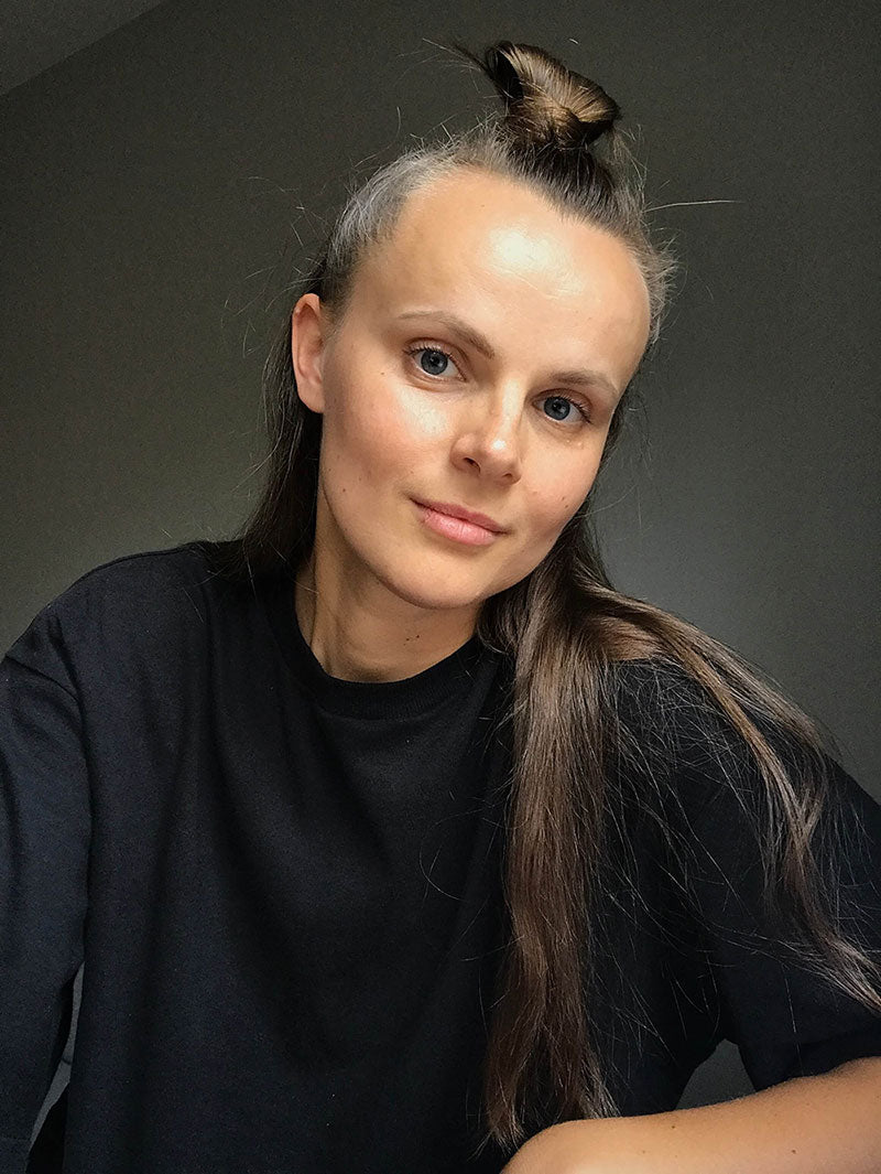 Portrait of a young woman with long brown hair wearing a black t-shirt, her head slightly tilted with a subtle smile.