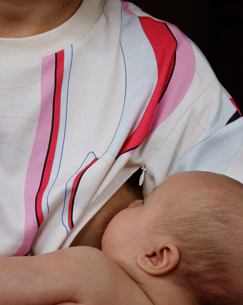 Mother breastfeeding in a colorful nursing t-shirt, showcasing comfortable, nursing-friendly clothing.