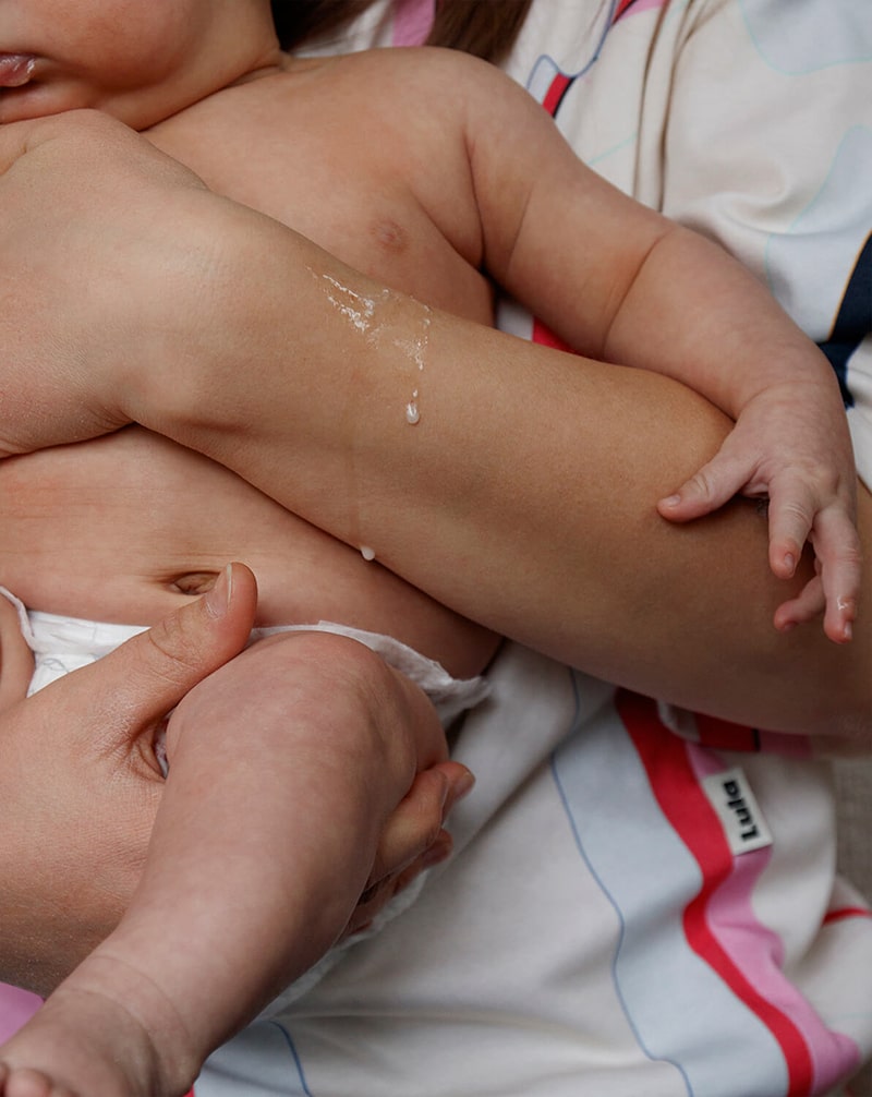 Mother holding her baby in a colorful nursing t-shirt, with mother's milk spit-up dripping from her hand.