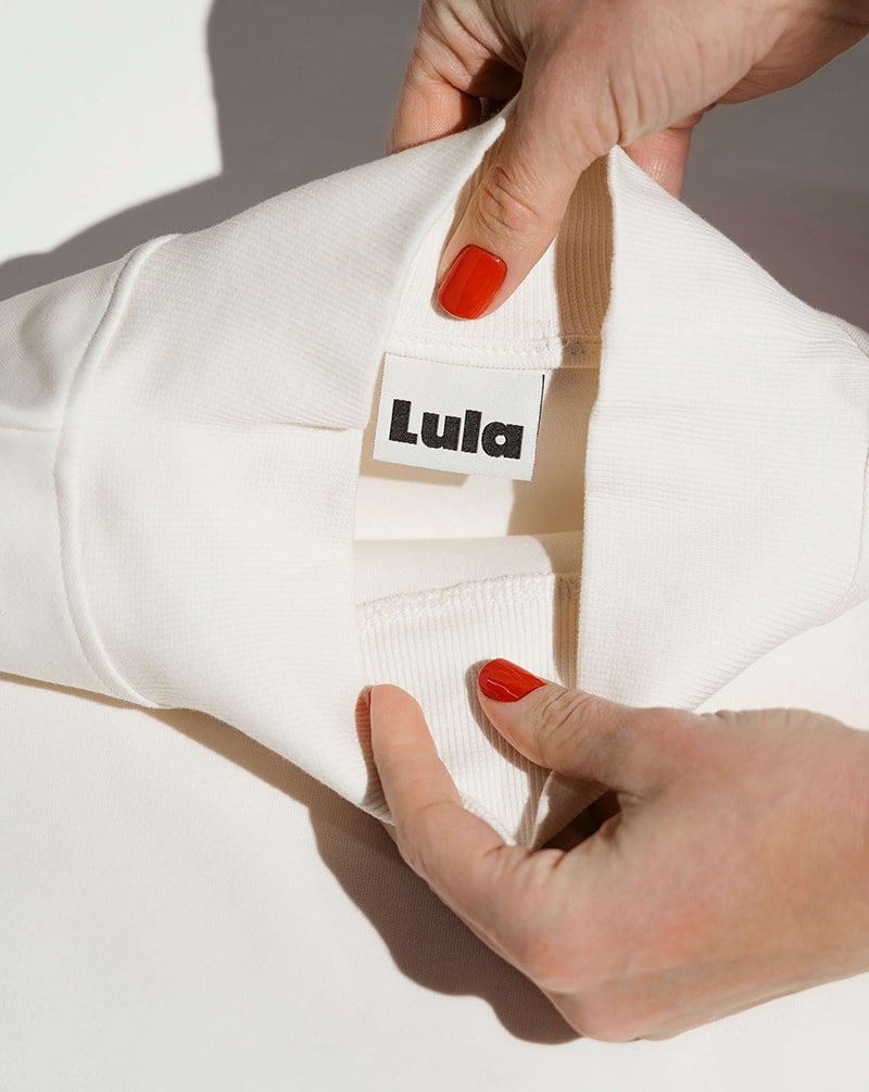 Close-up of the white nursing jumper's collar and the LULA brand label.