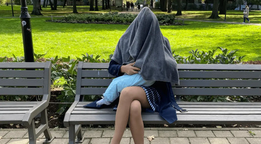 Mother sitting on a park bench discreetly breastfeeding her newborn while covered with a soft nursing blanket.