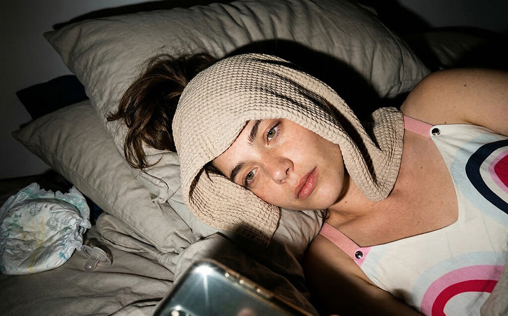 Mother is scrolling her phone whilst sleeping near diaper and pacifier.