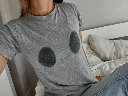 Woman wearing grey tee that has breast milk stains on it.