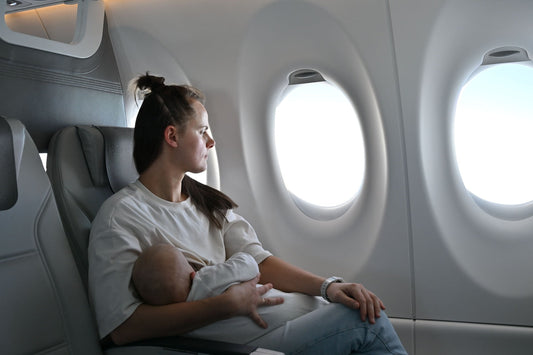Young mother breastfeeding her baby discreetly on an airplane, wearing a white nursing t-shirt, with baby in white clothes, bathed in soft daylight from the windows.