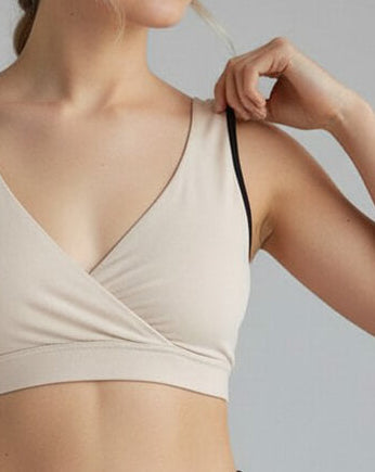 Woman wearing a beige sports bra and black leggings on a plain background