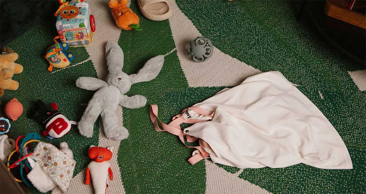 A messy kid’s room filled with toys scattered on the floor, with a dropped white nursing top.