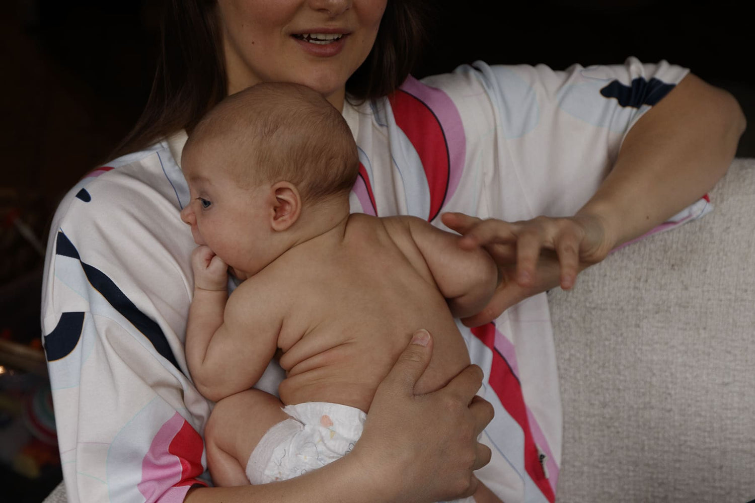 Mother wearing a colorful oversized nursing t-shirt, holding her naked baby close to her chest while having a conversation. Stylish and comfortable breastfeeding clothes for nursing moms.