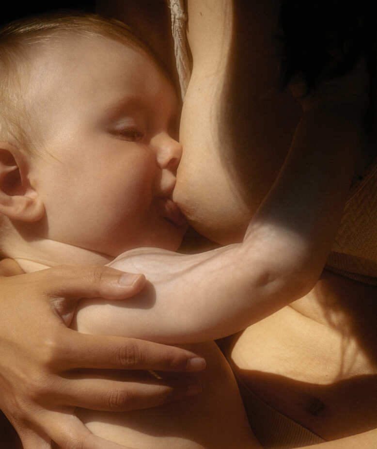 Close-up of skin-to-skin moment in natural sunlight, with a mother breastfeeding her baby. Intimate, nurturing scene highlighting the bond of breastfeeding.