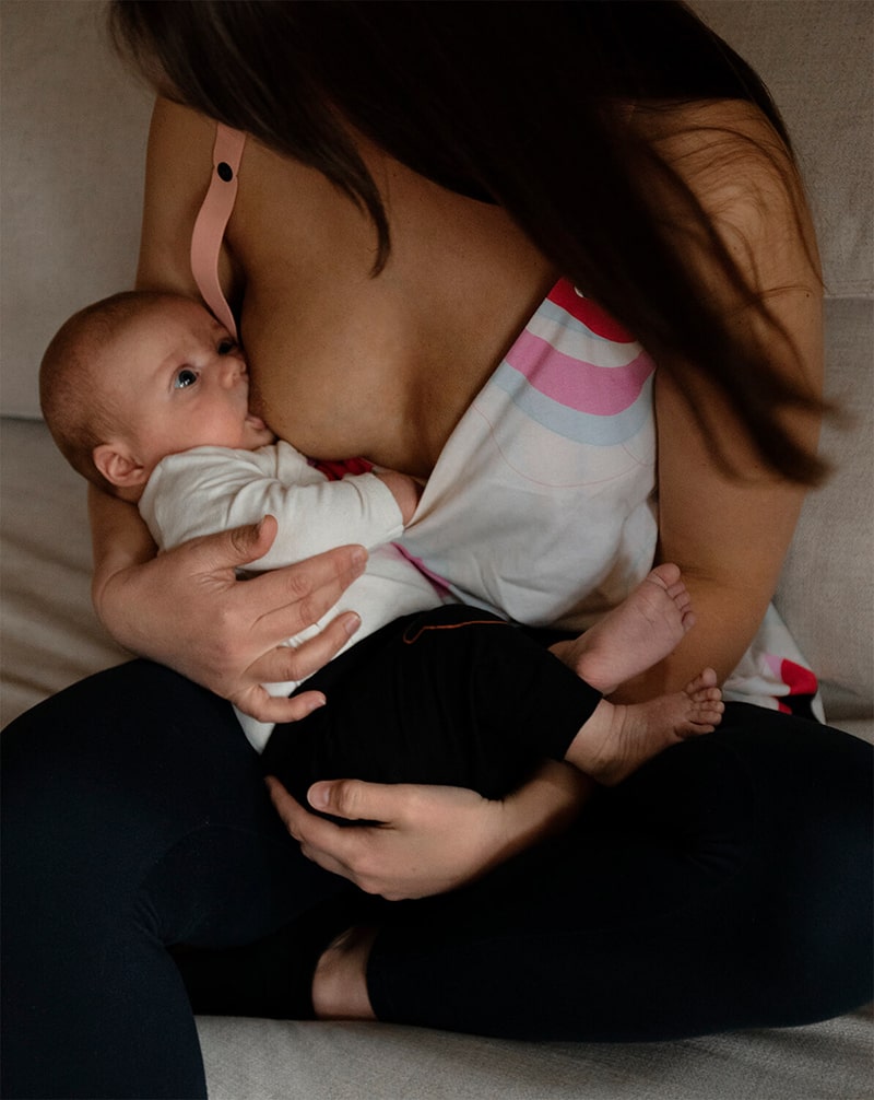 Mother sitting on a couch breastfeeding in a colorful nursing top, highlighting comfortable feeding.