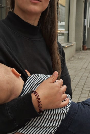 Mother wearing a black nursing jumper, sitting at an outdoor café by the street, discreetly breastfeeding her baby. Stylish and practical nursing clothes for breastfeeding moms on the go.