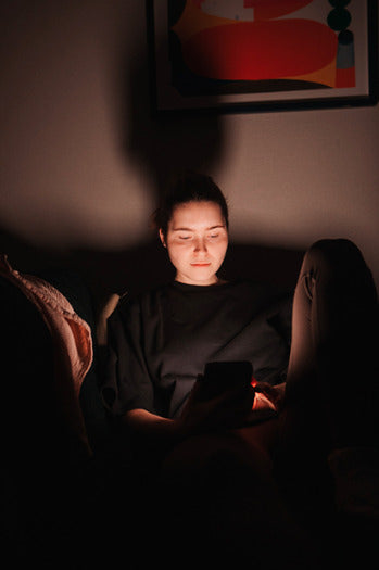 Young mom wearing a black nursing t-shirt, scrolling her phone in the middle of the night. Comfortable and practical nursing clothes for breastfeeding moms.