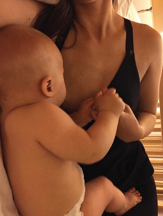 Close-up of a woman in a black nursing top lying in bed and breastfeeding her baby. Comfortable and practical breastfeeding clothes for nursing moms.