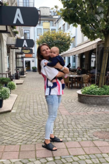 Young mother holding her baby close to her chest, showcasing a colorful nursing t-shirt while standing in the street. Modern and stylish breastfeeding clothes for nursing moms.