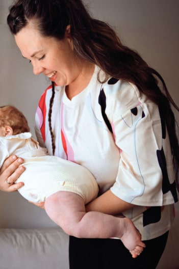Young mother lifting her baby while wearing a colorful nursing t-shirt. Modern and comfortable breastfeeding clothes for nursing moms.