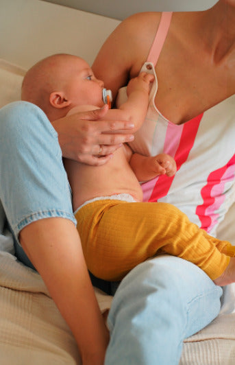 Mother holding her child while wearing a colorful nursing top with a built-in bra. Stylish and comfortable breastfeeding clothes for nursing moms.