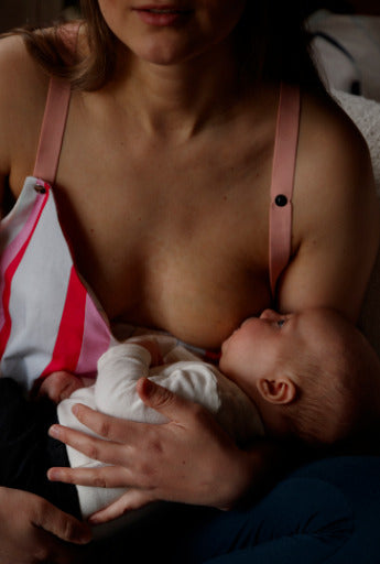 Close-up of mother breastfeeding her child while wearing a colorful nursing top with a built-in bra. Stylish and comfortable breastfeeding clothes for nursing moms.