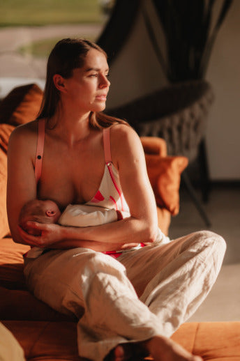 Mother breastfeeding her child while wearing a colorful nursing top with a built-in bra. Stylish and comfortable breastfeeding clothes for nursing moms.