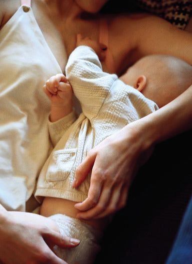 Close-up of a mother lying down and breastfeeding her baby while wearing a white cotton nursing top. Comfortable and breathable breastfeeding clothes for nursing moms.