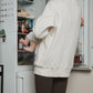 Mother in a white nursing sweater standing in front of an open refrigerator while breastfeeding her baby.