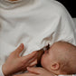 Mother breastfeeding in a white nursing jumper, showcasing comfortable, nursing-friendly clothing.
