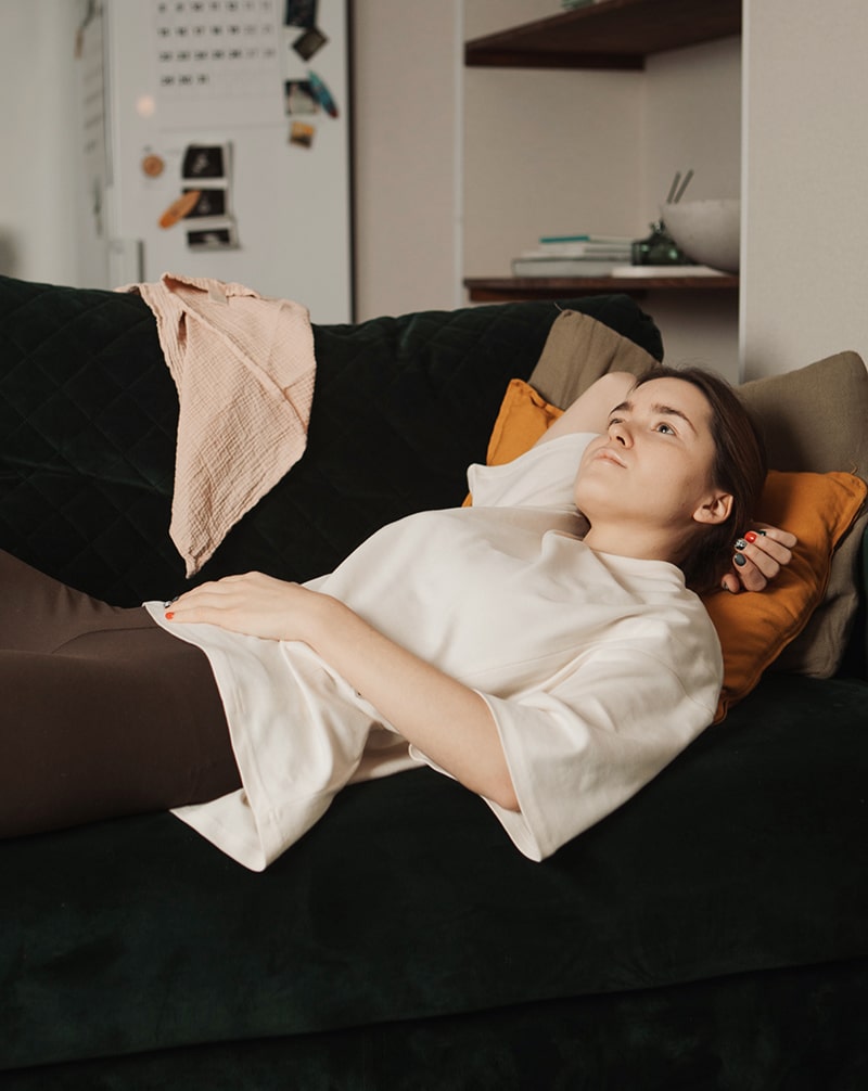 Mother relaxing on a couch in a white nursing t-shirt and leggings.