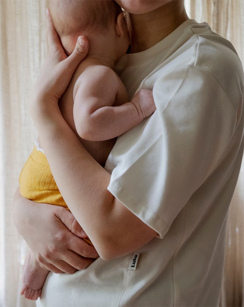 Mother holding her baby in a white nursing t-shirt, showcasing a sustainable nursing outfit.