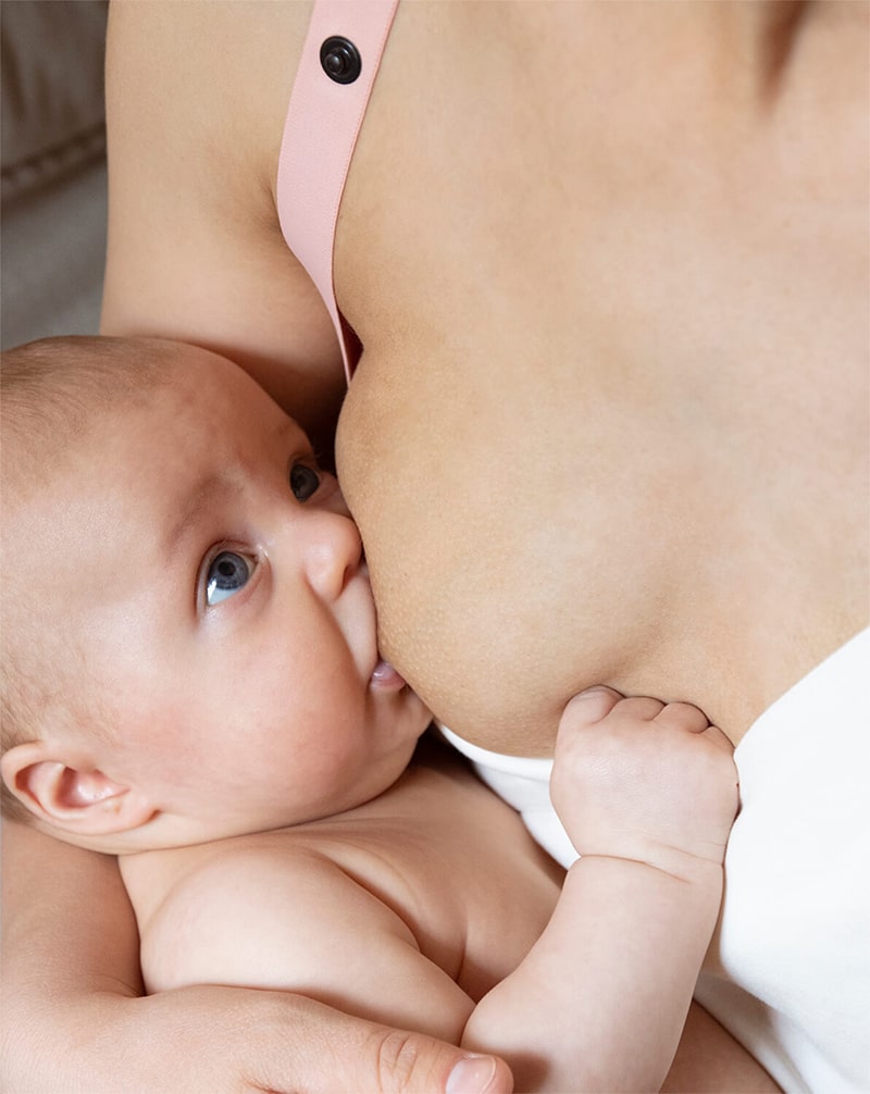 Close-up of a mother breastfeeding her baby in a white nursing top with pink shoulder straps.