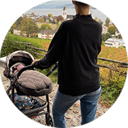 Young mother in a black jumper strolling her sleeping baby in a scenic outdoor setting.