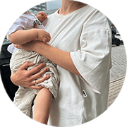 Mother in a white nursing t-shirt holds her baby against her chest with an urban city background