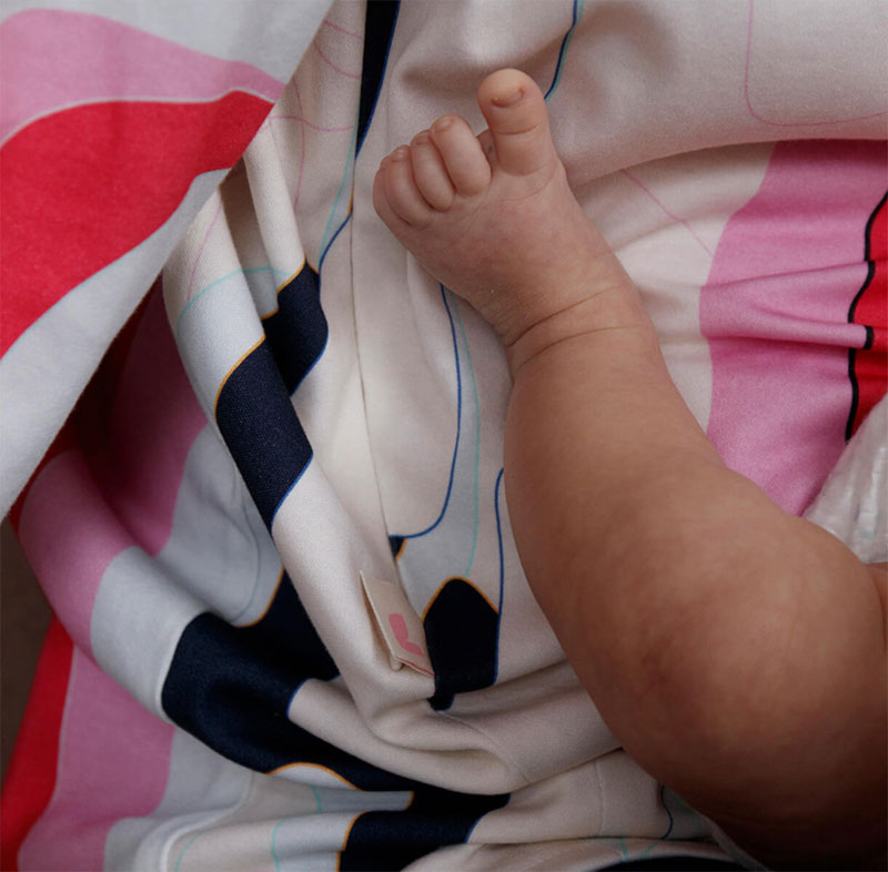 A baby's leg resting on a mother's stomach, wearing a colorful nursing t-shirt.