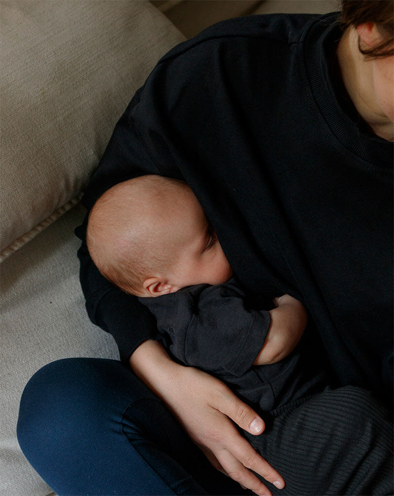 Mother breastfeeding in a black nursing jumper, highlighting nursing-friendly clothing.